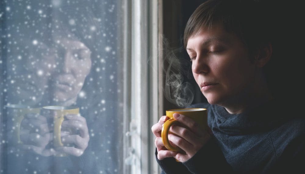 Woman sitting by a seasonal depression lamp with a fidget ring and cup of herbal tea for anxiety.