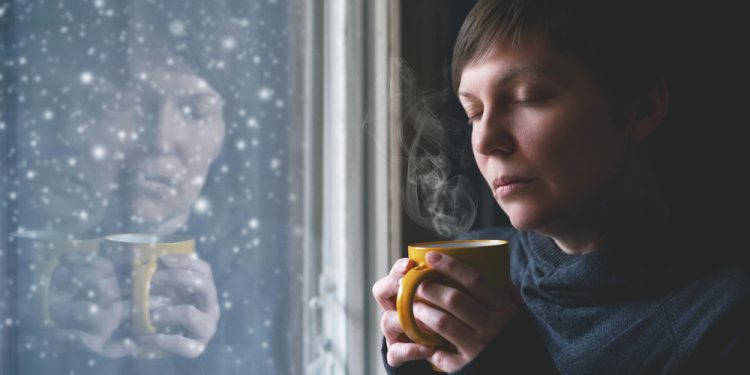 Woman sitting by a seasonal depression lamp with a fidget ring and cup of herbal tea for anxiety.