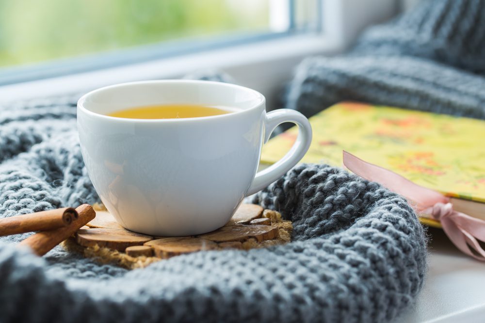 Cup of green tea for calmness with grey scarf on the windowsill.