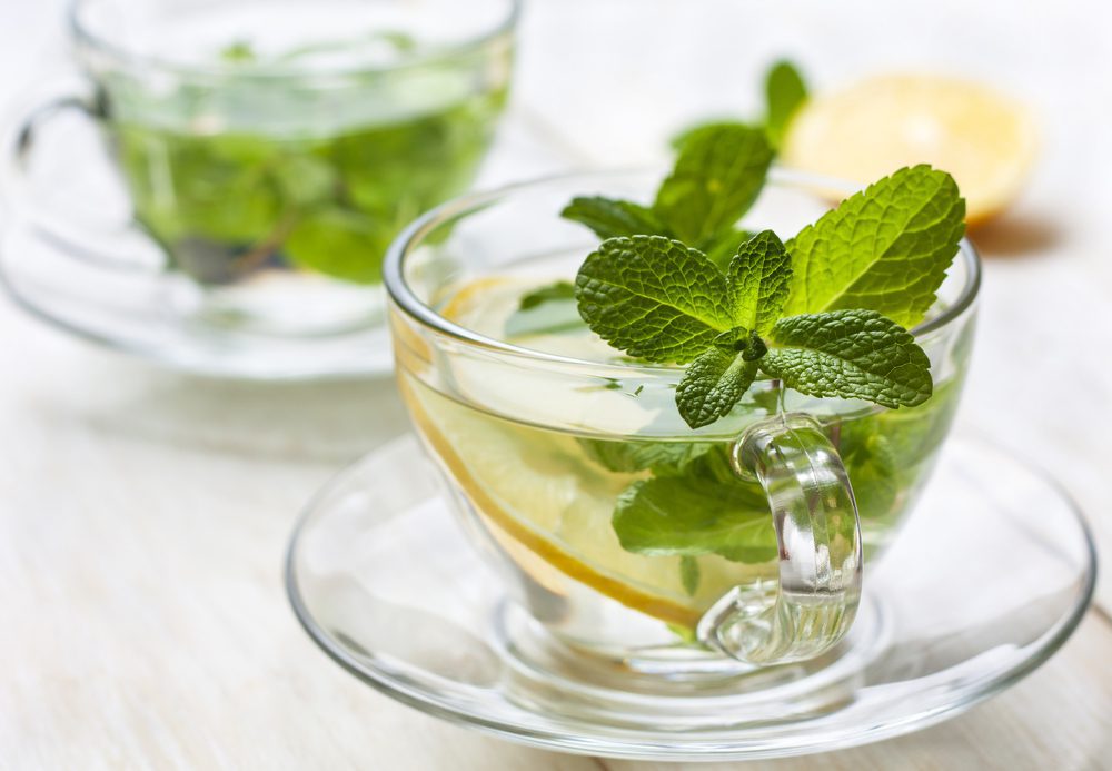 cups of tea with fresh mint and lemon slices on a blue wooden background