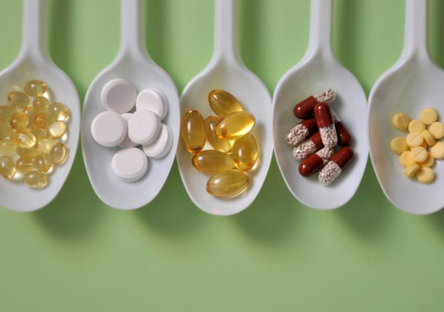 Tablets, capsules, dietary supplements, vitamins on white spoons. Medical background with best supplements for anxiety