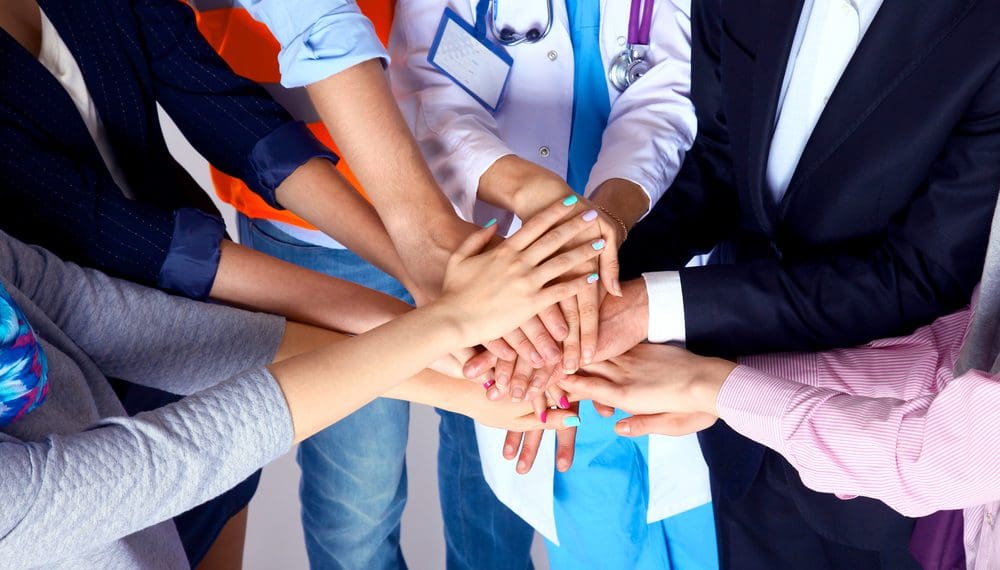Portrait of people with various occupations putting their hands on top of each other, such as public health officials and anxiety counselors