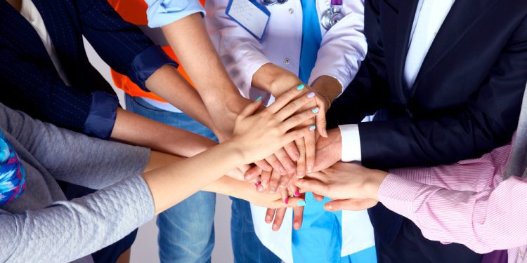 Portrait of people with various occupations putting their hands on top of each other, such as public health officials and anxiety counselors