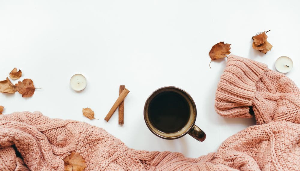 Knitted sweater, cup of coffee, autumn leaves, cinnamon sticks, candles on white background. Autumn composition for fall self care activities