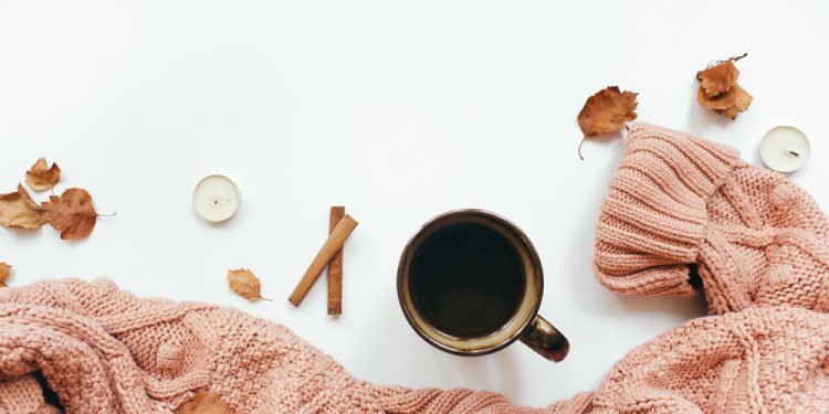 Knitted sweater, cup of coffee, autumn leaves, cinnamon sticks, candles on white background. Autumn composition for fall self care activities