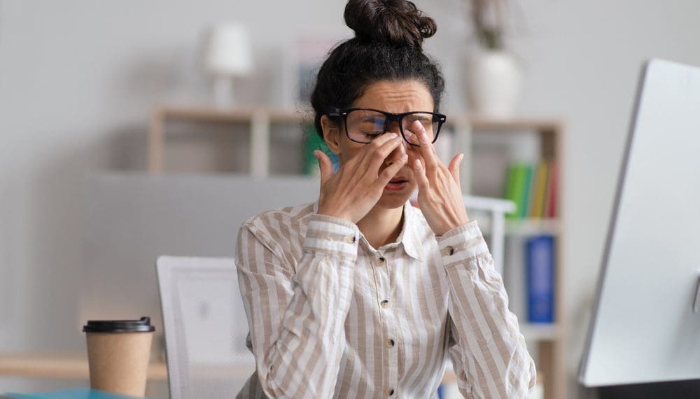 Female office worker in glasses rubbing tired eyes, exhausted from overworking, sitting at workplace in office, copy space. Young businesswoman feeling eye fatigue or pain, needing to learn how to deal with stress as a 911 dispatcher