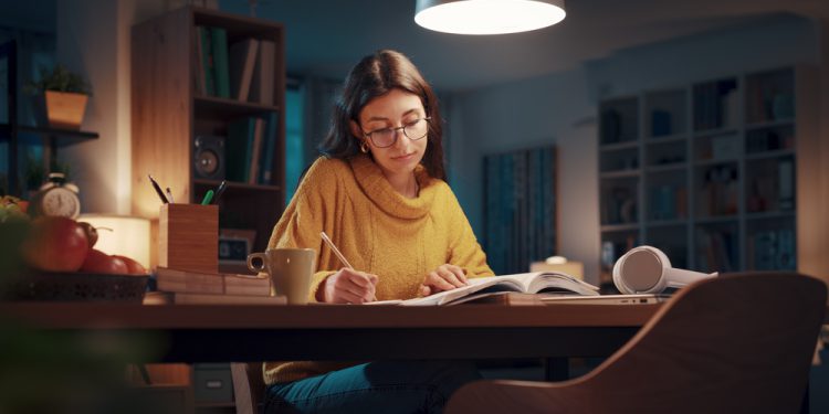 Young university student reading books late at night, she is studying and preparing for her exams, experiencing study stress and looking for study tips, such as fidget rings, worry stones and other spiritual gifts