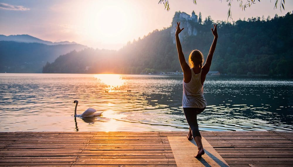 Person practicing yoga at sunrise on a dock, demonstrating calming strategies to manage anxiety with mindfulness and grounding techniques, like fidget rings