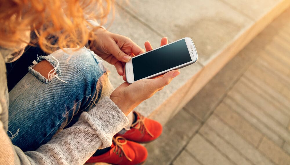 Person holding smartphone in one hand and a spinner ring in the other, symbolizing the connection between screen time and anxiety and the use of fidget tools for stress relief.
